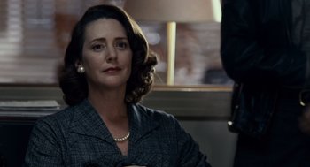 Movie still from “All the King's Men” (2006), directed by Steven Zaillian – A woman in a suit and pearl necklace sitting in front of a lamp; Close Up shot, Over the shoulder angle