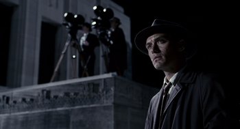 Movie still from “All the King's Men” (2006), directed by Steven Zaillian – A man wearing a hat standing in front of a building; Medium shot, Low angle