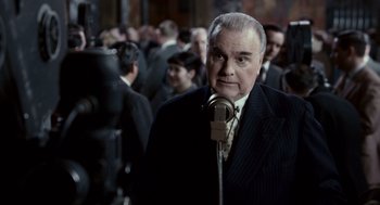 Movie still from “All the King's Men” (2006), directed by Steven Zaillian – An older man in a suit and tie is standing in front of a crowd; Medium shot, Over the shoulder angle