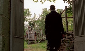 Movie still from “Tous les matins du monde” (1991), directed by Alain Corneau – A man in a black suit walking in front of a wooden structure; Wide shot, Over the shoulder angle