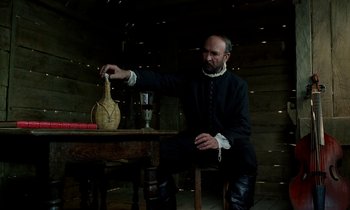 Movie still from “Tous les matins du monde” (1991), directed by Alain Corneau – A man sitting at a wooden table with a vase; Medium shot, Low angle