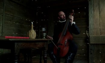 Movie still from “Tous les matins du monde” (1991), directed by Alain Corneau – A man playing an instrument while sitting at a table; Medium shot, Low angle