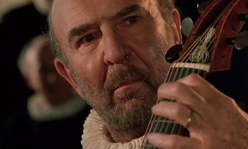 Movie still from “Tous les matins du monde” (1991), directed by Alain Corneau – An older man with a beard and mustache holding a guitar; Close Up shot, Over the shoulder angle
