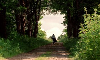 Movie still from “Tous les matins du monde” (1991), directed by Alain Corneau – A man walking down a dirt road through a forest; Extreme Wide shot, Low angle