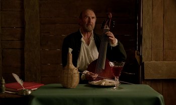 Movie still from “Tous les matins du monde” (1991), directed by Alain Corneau – A man sitting at a table holding a guitar; Medium shot, Low angle