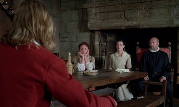 Movie still from “Tous les matins du monde” (1991), directed by Alain Corneau – A woman sitting at a table in front of a fireplace; Medium shot, Over the shoulder angle