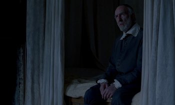 Movie still from “Tous les matins du monde” (1991), directed by Alain Corneau – An older man sitting on a bed in a dark room; Medium shot, Over the shoulder angle