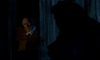 Movie still from “Tous les matins du monde” (1991), directed by Alain Corneau – A man sitting in front of a cross in a dark room; Medium shot, Over the shoulder angle