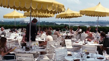 Movie still from “All the President's Men” (1976), directed by Alan J. Pakula – A group of people sitting at tables under yellow umbrellas; Wide shot, High angle