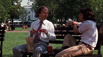Movie still from “All the President's Men” (1976), directed by Alan J. Pakula – Two men sitting on a park bench eating a sandwich; Medium shot, Over the shoulder angle