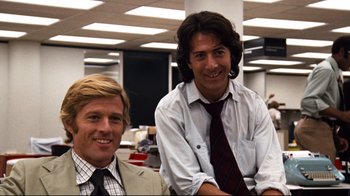 Movie still from “All the President's Men” (1976), directed by Alan J. Pakula – Two men are sitting in an office smiling for the camera; Medium shot, Low angle