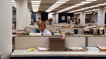 Movie still from “All the President's Men” (1976), directed by Alan J. Pakula – A man sitting at a cubicle desk in an office setting; Wide shot, Over the shoulder angle