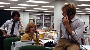Movie still from “All the President's Men” (1976), directed by Alan J. Pakula – A woman talking on a phone while sitting at a desk; Medium shot, Low angle