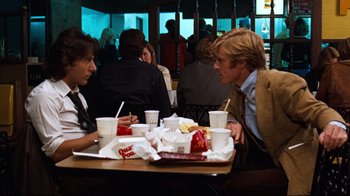 Movie still from “All the President's Men” (1976), directed by Alan J. Pakula – Two men are sitting at a table with drinks and food; Medium shot, Over the shoulder angle