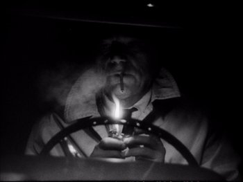 Movie still from “Alphaville” (1965), directed by Jean-Luc Godard – A man smoking a cigarette while holding a lit candle; Close Up shot, High angle