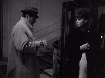 Movie still from “Alphaville” (1965), directed by Jean-Luc Godard – A man and a woman standing next to each other on steps; Medium shot, Over the shoulder angle