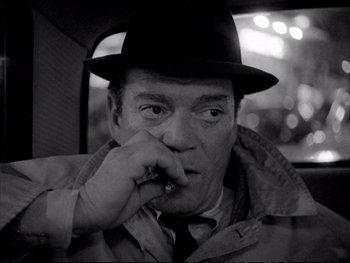 Movie still from “Alphaville” (1965), directed by Jean-Luc Godard – A black and white photo of a man smoking a cigarette in the back of a car; Close Up shot, Over the shoulder angle