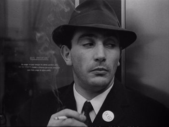 Movie still from “Alphaville” (1965), directed by Jean-Luc Godard – A black and white photo of a man smoking a cigarette; Close Up shot, Low angle