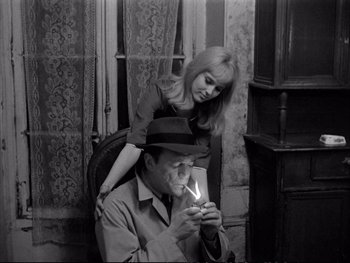 Movie still from “Alphaville” (1965), directed by Jean-Luc Godard – A man and a woman are holding a lit cigarette; Medium shot, High angle