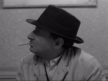 Movie still from “Alphaville” (1965), directed by Jean-Luc Godard – A black and white photo of a man smoking a cigarette; Close Up shot, Low angle