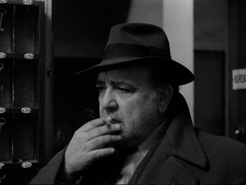 Movie still from “Alphaville” (1965), directed by Jean-Luc Godard – A black and white photo of a man smoking a cigarette; Close Up shot, Low angle