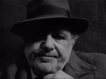 Movie still from “Alphaville” (1965), directed by Jean-Luc Godard – Black and white photograph of a man wearing a hat; Close Up shot, Low angle