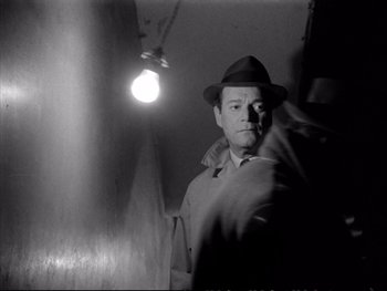 Movie still from “Alphaville” (1965), directed by Jean-Luc Godard – A black and white photo of a man in a hat; Medium shot, Low angle