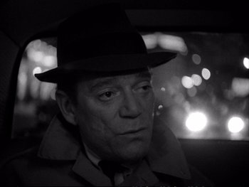 Movie still from “Alphaville” (1965), directed by Jean-Luc Godard – A black and white photo of a man wearing a hat; Close Up shot, Over the shoulder angle
