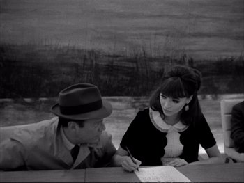 Movie still from “Alphaville” (1965), directed by Jean-Luc Godard – A man and a woman sitting next to each other at a table; Medium shot, High angle