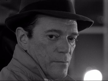 Movie still from “Alphaville” (1965), directed by Jean-Luc Godard – An older man wearing a hat and a jacket; Close Up shot, Low angle
