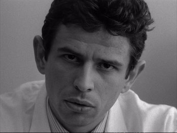 Movie still from “Alphaville” (1965), directed by Jean-Luc Godard – Black and white photograph of a man in a white shirt; Close Up shot, Low angle