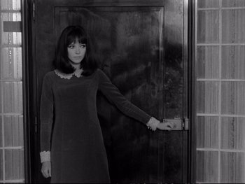 Movie still from “Alphaville” (1965), directed by Jean-Luc Godard – A woman standing in front of an open door; Medium shot, High angle