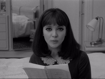 Movie still from “Alphaville” (1965), directed by Jean-Luc Godard – A woman sitting in front of a mirror reading a book; Close Up shot, High angle