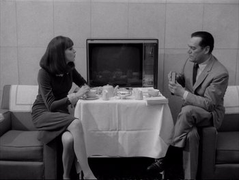 Movie still from “Alphaville” (1965), directed by Jean-Luc Godard – A man and a woman sitting at a table with cups; Medium shot, High angle