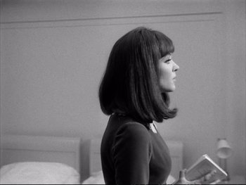 Movie still from “Alphaville” (1965), directed by Jean-Luc Godard – A black and white photo of a woman with a book; Medium shot, Over the shoulder angle