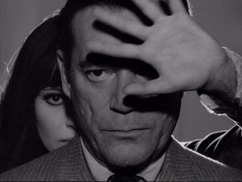 Movie still from “Alphaville” (1965), directed by Jean-Luc Godard – A man and a woman standing next to each other; Close Up shot, High angle