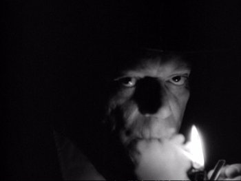Movie still from “Alphaville” (1965), directed by Jean-Luc Godard – A man is holding a candle in the dark; Extreme Close Up shot, Low angle