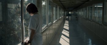 Movie still from “Alps” (2011), directed by Yorgos Lanthimos – A person standing in front of a window in a building; Medium shot, Low angle