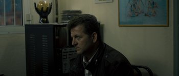 Movie still from “Alps” (2011), directed by Yorgos Lanthimos – A man sitting in front of a television in a room; Medium shot, Over the shoulder angle