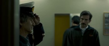 Movie still from “Alps” (2011), directed by Yorgos Lanthimos – A man wearing a hat standing next to a door; Close Up shot, Over the shoulder angle