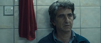 Movie still from “Alps” (2011), directed by Yorgos Lanthimos – A person standing in front of a wall; Close Up shot, Over the shoulder angle