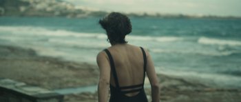 Movie still from “Alps” (2011), directed by Yorgos Lanthimos – A woman standing on the beach looking out at the ocean; Medium shot, Over the shoulder angle