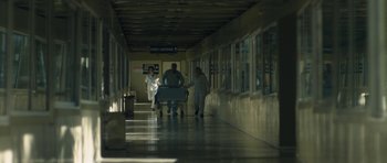 Movie still from “Alps” (2011), directed by Yorgos Lanthimos – A group of people walking down a hallway with a cart; Extreme Wide shot, Low angle