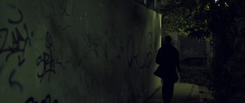 Movie still from “Alps” (2011), directed by Yorgos Lanthimos – A person walking in front of a wall covered in graffiti; Wide shot, Low angle