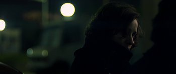 Movie still from “Alps” (2011), directed by Yorgos Lanthimos – A person with dark hair is standing in front of a bright light; Close Up shot, Over the shoulder angle