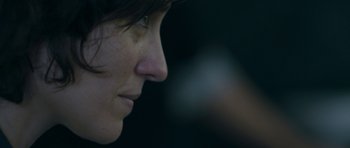 Movie still from “Alps” (2011), directed by Yorgos Lanthimos – A woman's face with a blurry background; Extreme Close Up shot, Over the shoulder angle