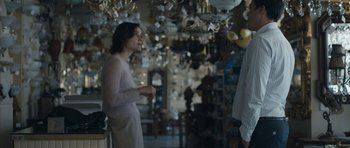 Movie still from “Alps” (2011), directed by Yorgos Lanthimos – A woman standing next to a man in a room full of chandeliers; Medium shot, Over the shoulder angle