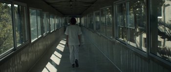 Movie still from “Alps” (2011), directed by Yorgos Lanthimos – A person walking down a long hallway in a building; Wide shot, Low angle