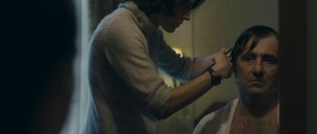 Movie still from “Alps” (2011), directed by Yorgos Lanthimos – A man in a gray sweater is writing on a piece of paper; Close Up shot, Over the shoulder angle