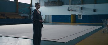 Movie still from “Alps” (2011), directed by Yorgos Lanthimos – A woman standing in a gym holding a hula hoop; Medium shot, Low angle